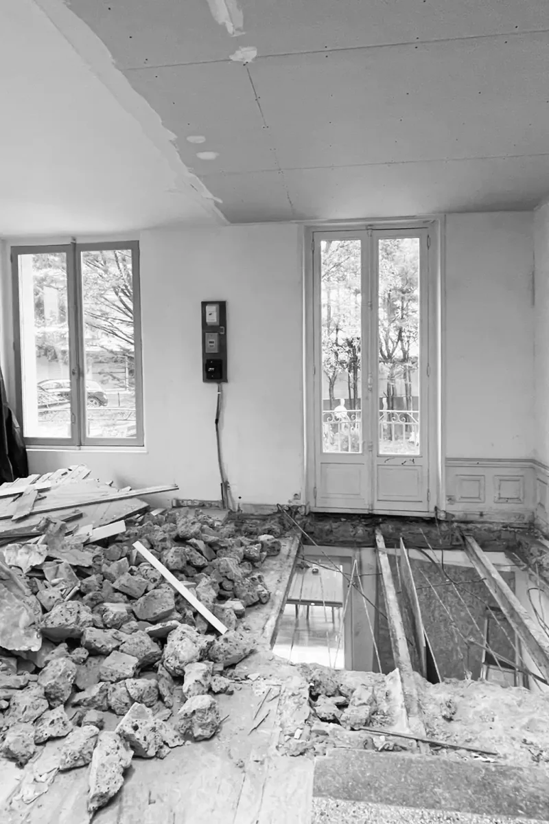 Chantier de rénovation en noir et blanc montrant la démolition lourde du plancher d'une maison ancienne.