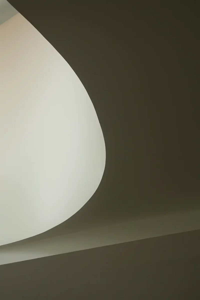 Photographie minimaliste de la courbe blanche d'un escalier sur fond d'ombre.