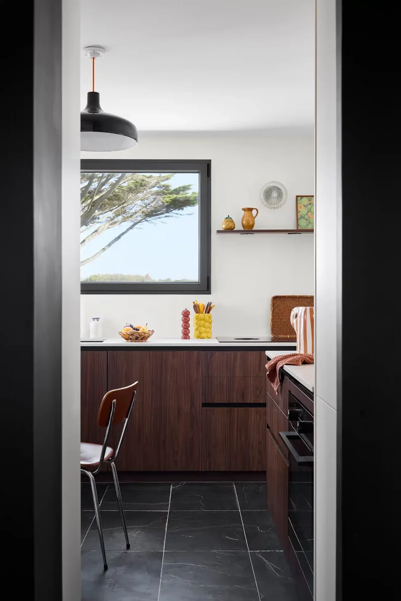 Vue depuis une arche blanche vers la cuisine moderne en bois de pin et plan de travail noir.