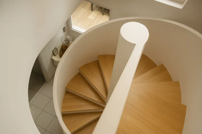 Gros plan zénithal sur le départ de la main courante blanche et les marches en chêne de l'escalier.