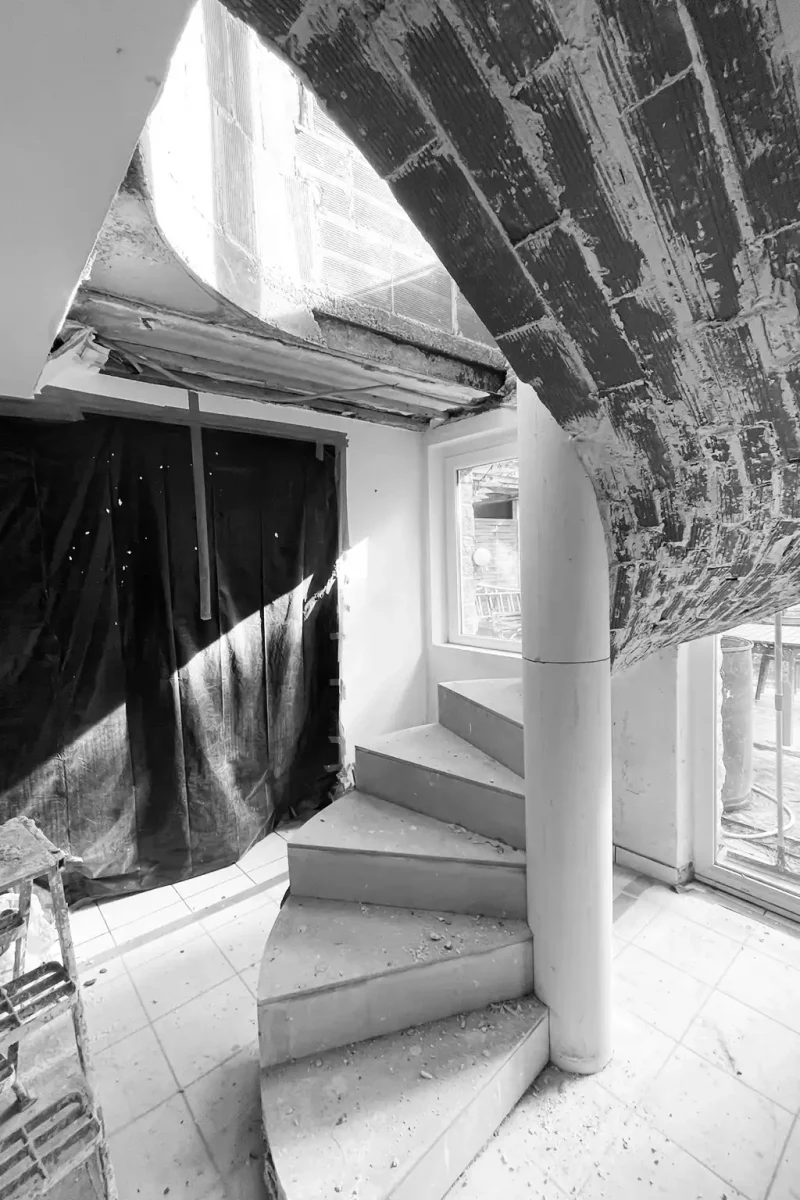 Structure brute d'un escalier hélicoïdal en cours de montage sur un chantier en noir et blanc.