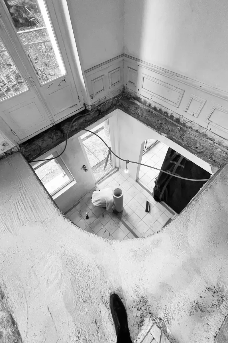 Vue du dessus en noir et blanc montrant l'installation de l'ossature d'un escalier en colimaçon.