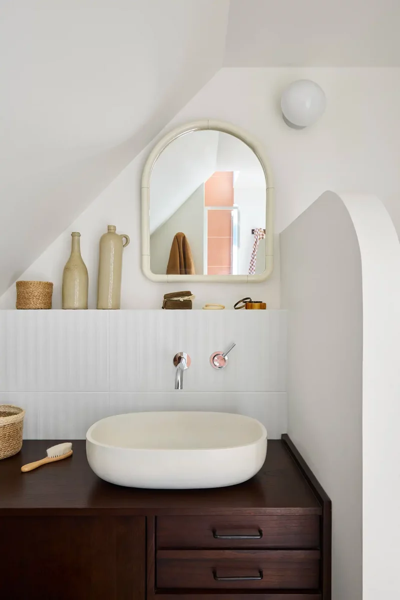 Salle de bain épurée avec vasque à poser blanche sur meuble en bois sombre et miroir en arche.