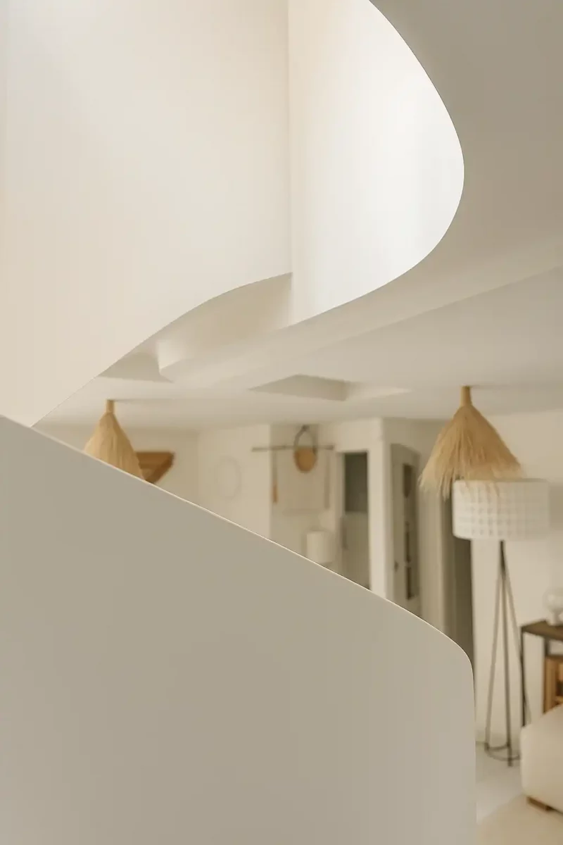 Vue en contre-plongée de la sous-face courbe d'un escalier blanc en staff dans un salon.
