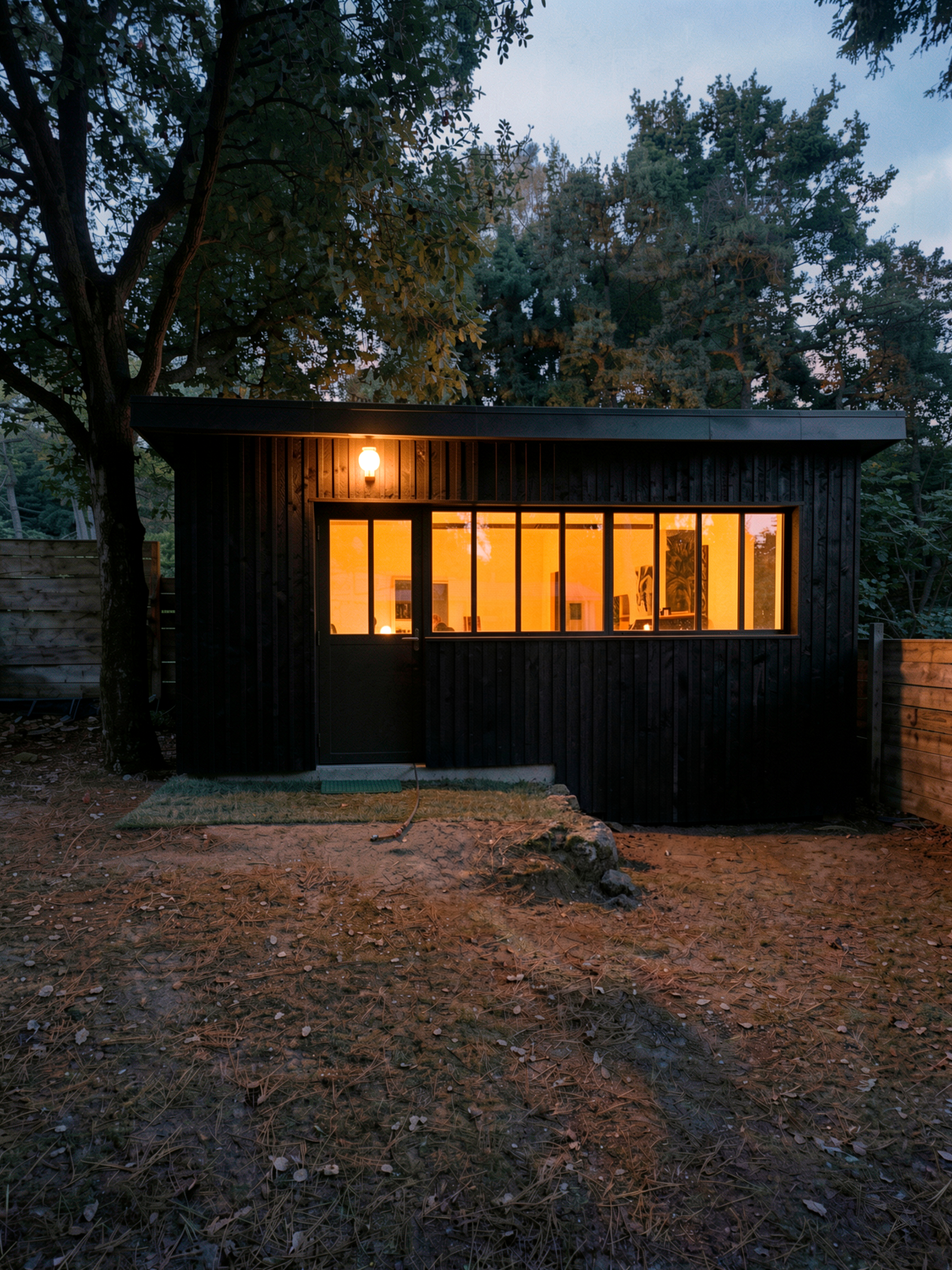 Atelier de jardin à la tombée du jour — La Baule Atelier de jardin en bois brûlé à la tombée du jour à La Baule, lumière chaude par la baie vitrée